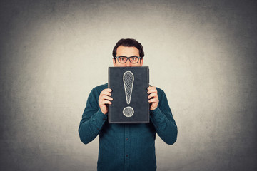 Shocked businessman looking astonished with big eyes, holding a board with a drawn exclamation mark...