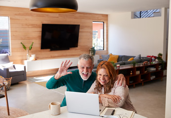 Senior Hispanic Couple At Home With Laptop Having Video Chat With Family