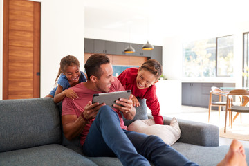 Children Creeping Up And Surprising Father Using Digital Tablet At Home