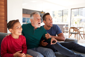 Excited Multi-Generation Male Hispanic Family Sitting On Sofa At Home Watching Sports On TV
