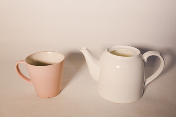 
pink cup and white ceramic teapot on a white background