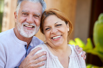 Portrait Of Smiling Senior Hispanic Couple Relaxing In Garden At Home Together