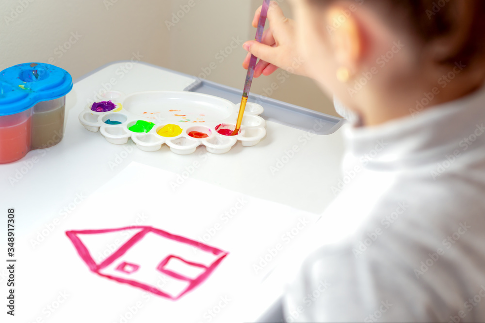 Wall mural Little girl is painting house on the white paper with red watercolor. Drawing time.