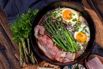 Delicious breakfast lunch branch of fried eggs, bacon, green asparagus, greenery and parmesan cheese on pan.