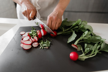Female hands cut radish into circles on a wooden board close-up,cooking vegetarian salad