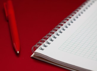 Notebook and red pen on the red cover of the laptop, all in red colors