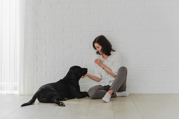 Cute young woman kisses and hugs her black labrador. Love between owner and dog. Isolated over white background. Studio portrait.