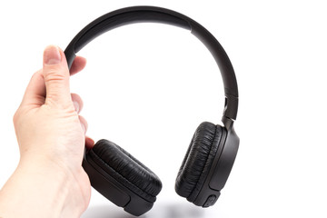 Fototapeta na wymiar Black wireless headphones in hand on white background. Advanced acoustic stereo sound system