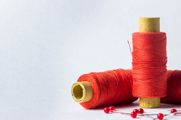 Three spools of scarlet thread. Nearby are needles with scarlet heads. Photo on a white background