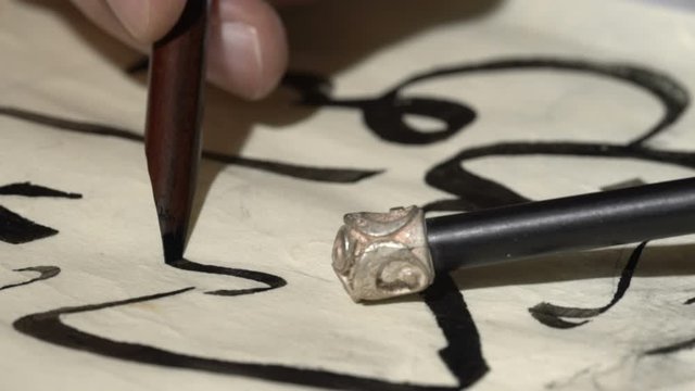 calligrapher writes arabic lettering with calligraphy pen on parchment. macro shot of islamic calligraphy art. close up slider dolly shot in calligrapher workshop table
