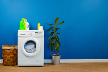 Washing machine with laundry on blue wall background, close up.