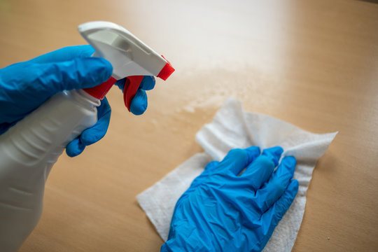 Cleaning home table sanitizing office table surface with disinfectant spray bottle washing surfaces with towel and gloves. COVID-19 prevention sanitizing inside.