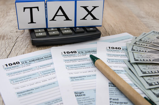 tax forms 1040 with dollars and calculator on a wooden background. The inscription "tax" on the cubes. Close-up.