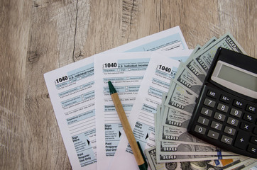 tax forms 1040 with calculator, pen and dollars on a wooden table