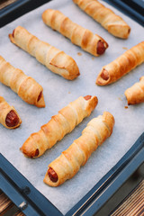 Baked sausage rolls on the baking sheet on the wooden table. Hot dogs. Sausage in the dough.