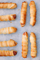 Baked sausage rolls on the baking sheet on the wooden table. Hot dogs. Sausage in the dough.