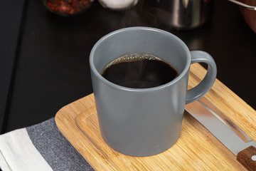 Cup of hot coffee on wooden board on kitchen table close up