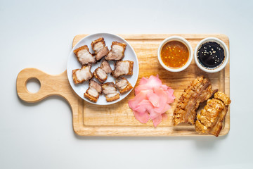 Deep Fried Crispy Streaky Pork Belly Thai and Chinese Food on Cutting Board with Sauce and Ginger on White Background Isolated.