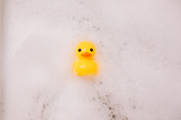 Yellow rubber duck in the bath with bubble foam