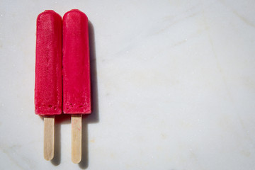 Two red pink popsicles sitting on a white marble slab