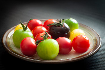 Fresh, colorful red, green, yellow and purple tomatoes served on a rustic dish.