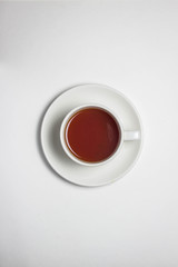 A cup of tea in a white glass and on a saucer on a white tablecloth. A cup of tea is located in the middle of the photo.