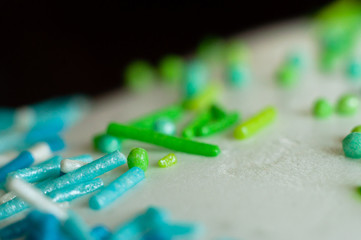 Decorative confectionery balls and sticks of green and blue decorate the white glaze of festive baking. Easter cake close-up, macro shot.