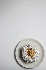 Cake with white cream and nut crumbs on a white saucer. The cake is located on the right below in the photo