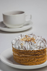 Cake with white cream and nut crumbs on a white saucer. Behind a cup of tea