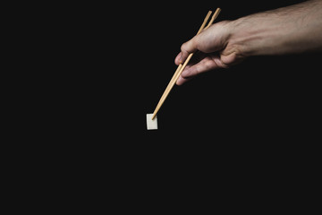 Hand holds sugar cube with Chinese chopsticks on black background