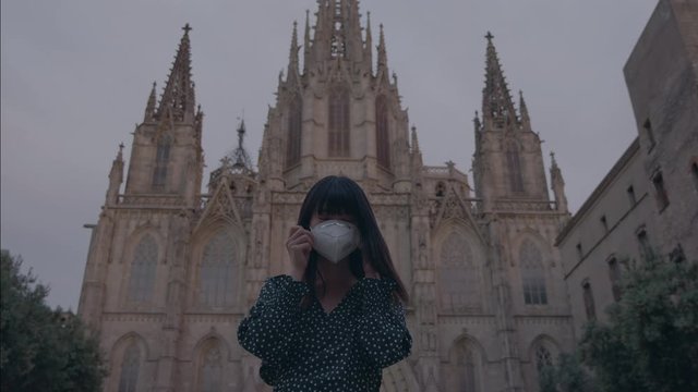In a pandemic emergency a japanese girl puts and takes off a mask in Barcelona city in front of Cathedral 4K