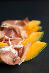 Food concept, prosciutto, ham with fresh melon on a dark background, top view with copy space, with space for your text, italiano snack, flat lay, honey melon or cantaloupe