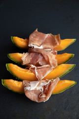 Food concept, prosciutto, ham with fresh melon on a dark background, top view with copy space, with space for your text, italiano snack, flat lay, honey melon or cantaloupe