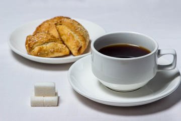 Confectionery baking and a cup of coffee on a white tablecloth. Nearby are three cubes of sugar. Tea set is also white