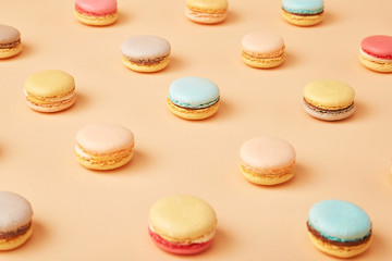 Macaroons on colored background, a pattern of colorful french cookies macarons. Beige, brown french cookies macarons on yellow peach background. Gift for Valentine's Day