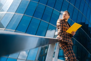 A young businessman stands on a blue background in a business suit holding documents. The concept of meeting businessmen ©  drugoenebo