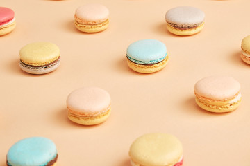 Macaroons on colored background, a pattern of colorful french cookies macarons. Beige, brown french cookies macarons on yellow peach background. Gift for Valentine's Day