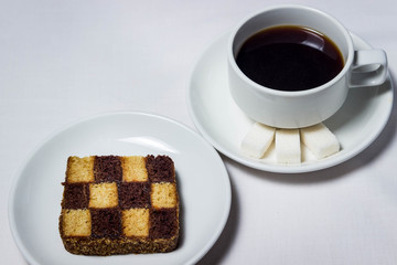 Chess baking and a cup of coffee on a white tablecloth. Tea set is also white