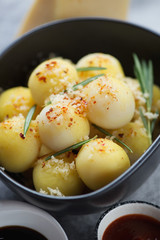 Close-up of baked potato balls topped with grated cheese and rosemary, selective focus, vertical shot