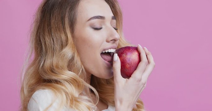 Girl biting red apple and widely smiling, close up portrait