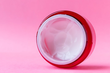 Round open red plastic jar with with white cream inside on a pink background with copy space. Skin care, cosmetics concept. Beauty packaging template. Side closeup view