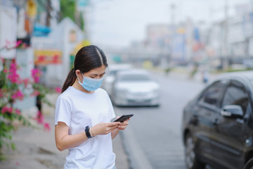 Asian woman wearing an anti-virus mask and standing using a smartphone to communicate while outside.