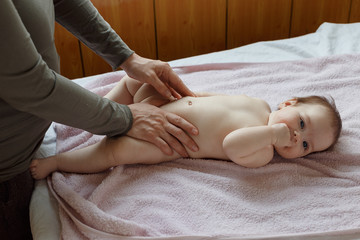 Top view of mother and her cute child on bed. Baby massage and exercises of gymnastics.