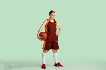 Young caucasian female basketball player confident holding ball, posing isolated on mint colored background. Concept of sport, movement, energy and dynamic, healthy lifestyle. Training, practicing.