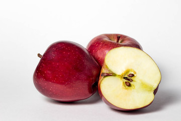 Three apples on a white background. Two apples are whole. the third apple is cut in half
