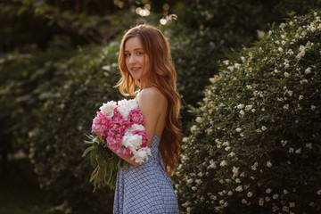 portrait of a girl with peonies. model is smiling. cosmetics and beautician. blurred background, art effect. weekend summer walk
