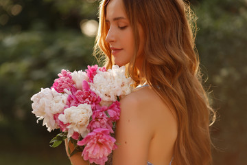 Fototapeta premium girl in the sun. Close-up portrait of a model with flowers in the summer. walk in the park in spring. cosmetics and beautician. blurred background, art effect. peonies. summer flowers