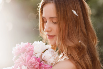 Naklejka premium Close-up portrait of a model with flowers in the summer at sunset. girl with peonies. blurred background, concept