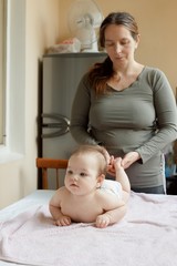 mother stands next to the child. Massage for the baby. Four month old baby smiling doing gymnastics