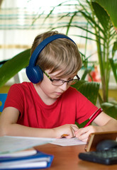 blond boy does homework at the table in headphones